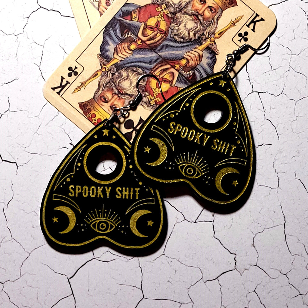 Black acrylic planchette earrings with gold Spooky Shit lettering, moons and eye