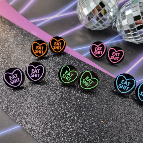 Round black stud earrings with neon heart outline and Eat Shit lettering