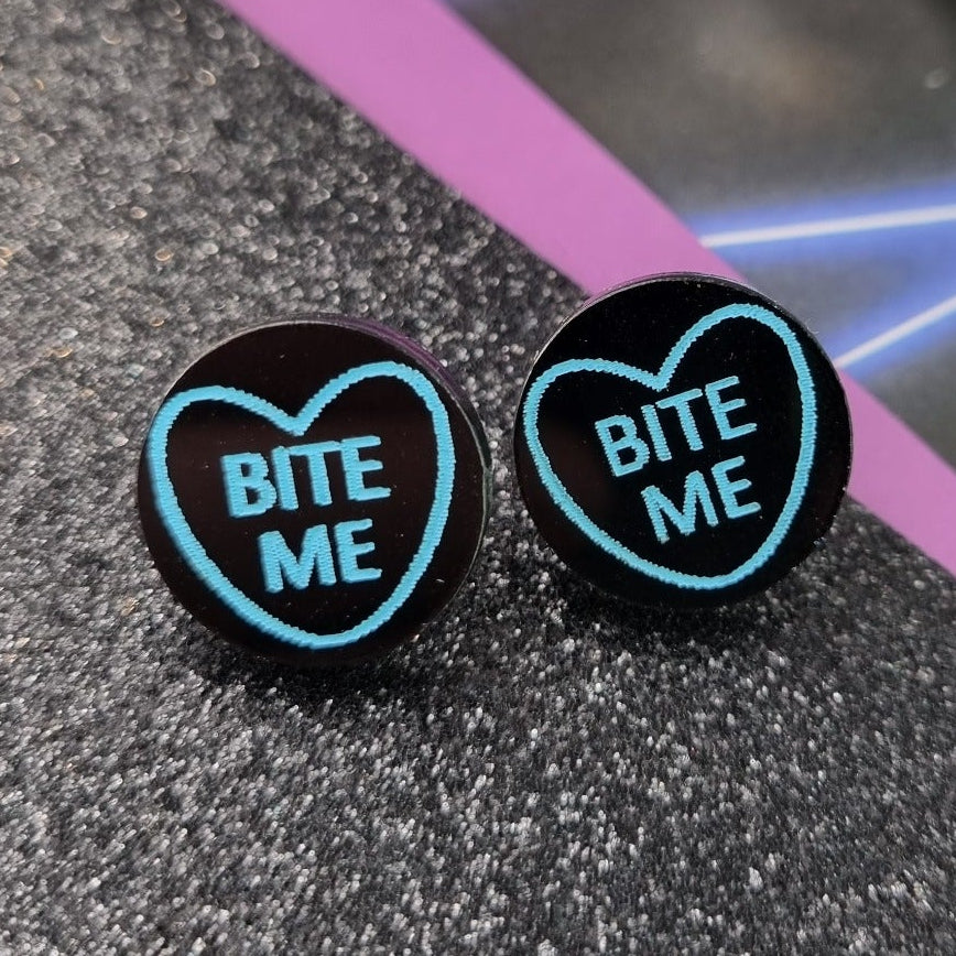 Round black stud earrings with neon heart outline and Bite Me lettering, view 2