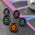 Round black stud earrings with neon heart outline and Bite Me lettering