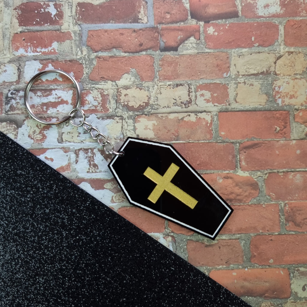 Black acrylic coffin keyring with white outline and gold cross