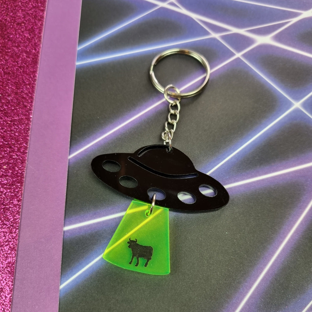 Black UFO keyring with neon green tractor beam and cow silhouette