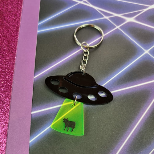 Black UFO keyring with neon green tractor beam and cow silhouette